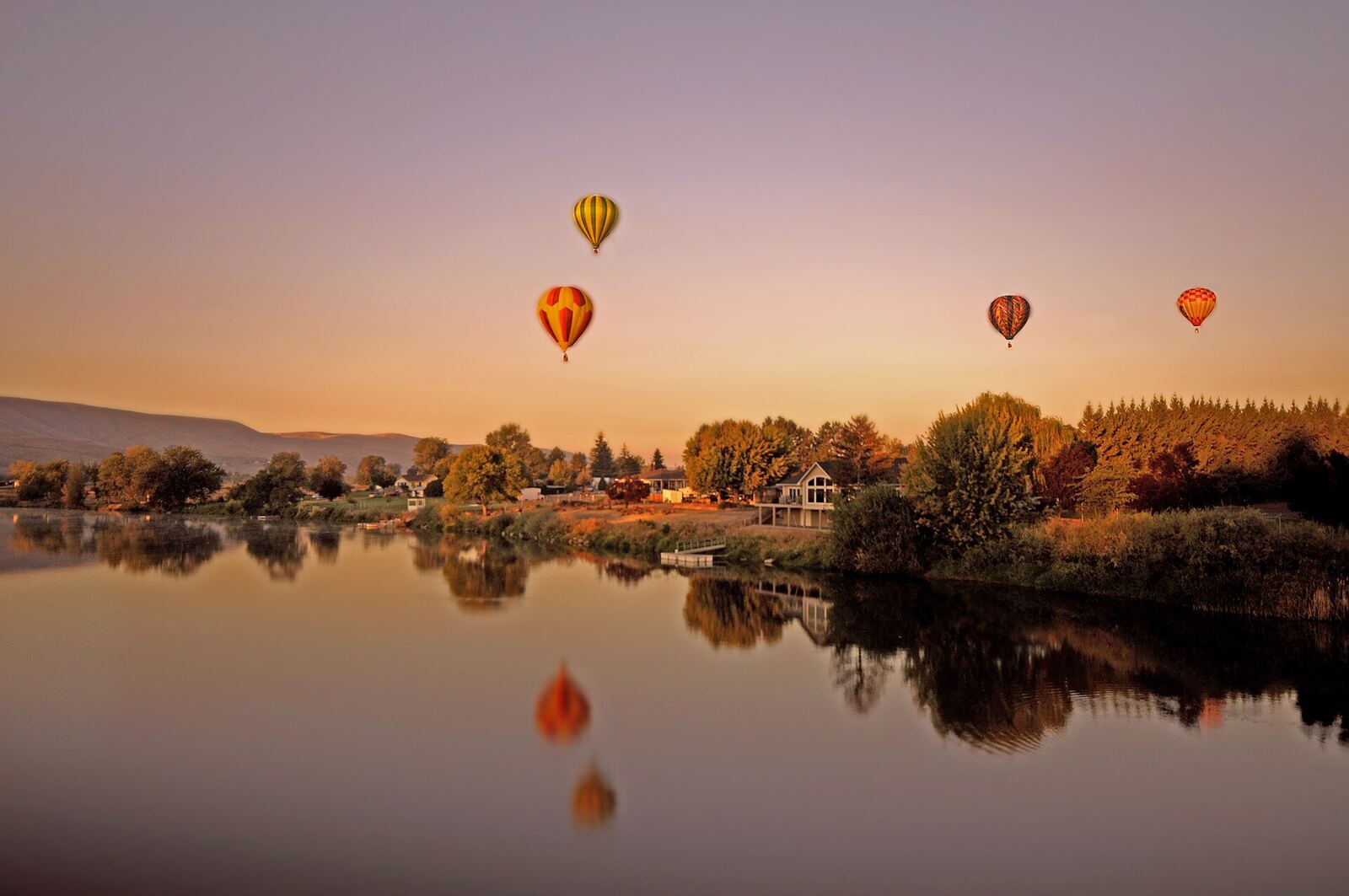 Hot air balloons drifting over the Yakima River at sunrise during the Prosser Balloon Rally